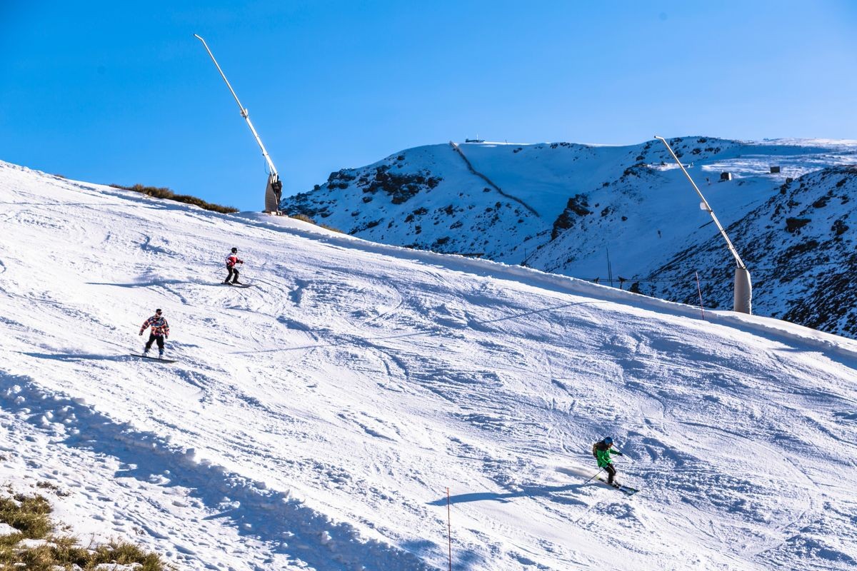 Skiers in sports clothing skiing on snowy mountainside of Sierra Nevada mountain in Spain region on sunny day with clear blue sky