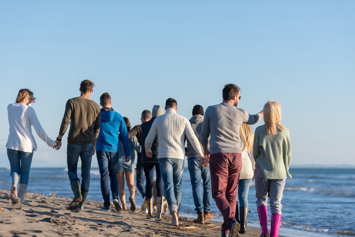 group of young friends spending day together running on the beach during autumn day